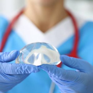 Gloved doctor holds female breast implant in his hands. Plastic surgery and mammoplasty concept